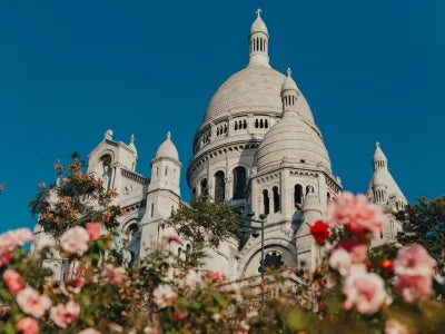 White cathedral with domes against blue sky, pink flowers in foreground, travel destination